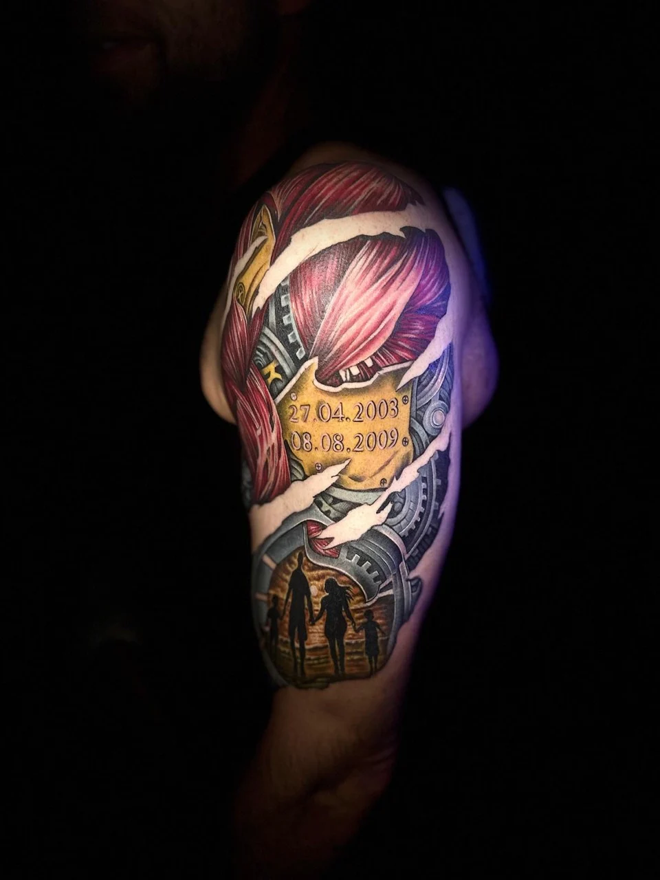 Farbiges Biomechanik-Tattoo mit Zahnrädern und Familiensilhouetten am Oberarm von Dominik Stegner – noch in Arbeit